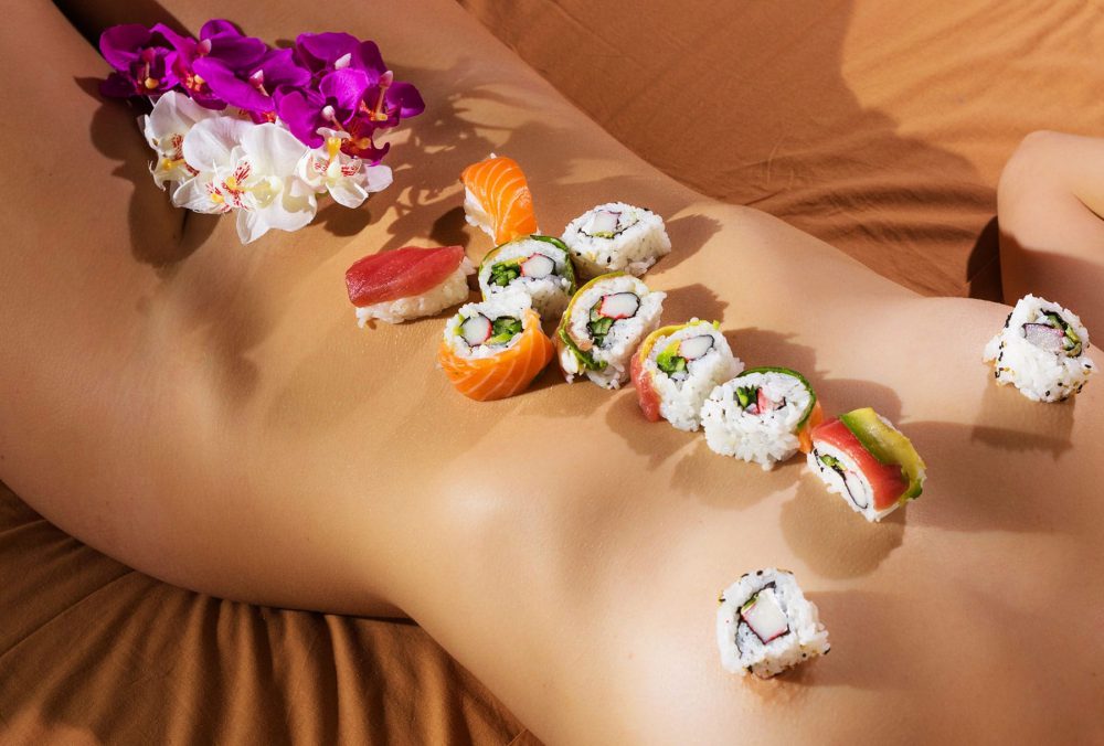 Naked body of a woman covered in different types of sushi.