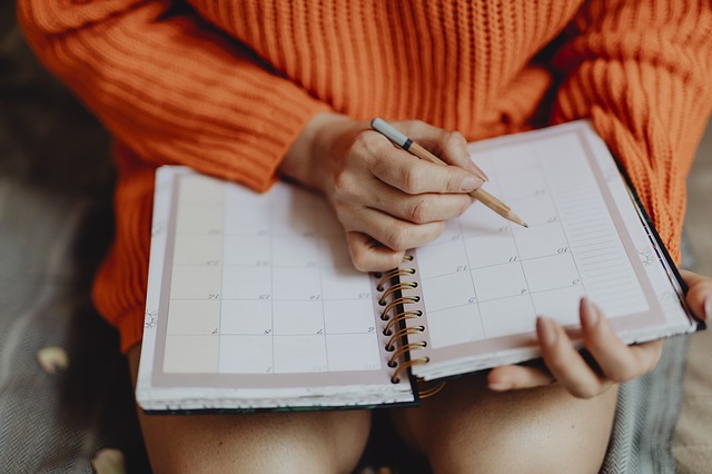 A woman wearing an orange winter jumper dress checking dates in her diary with a pencil